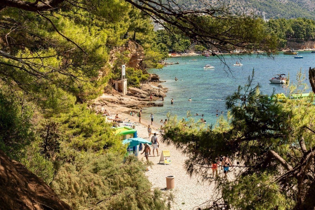 Belebter Strand mit Wassersport-Station und Liegen entlang der Küste